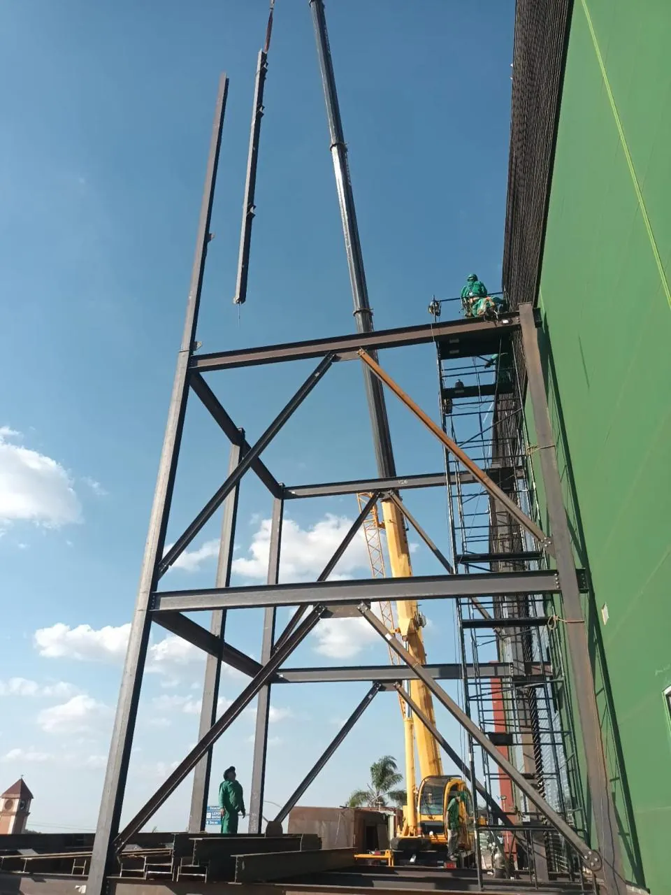Estrutura metálica do elevador de carga em montagem junto à fachada do BH Outlet, com guindaste ao fundo