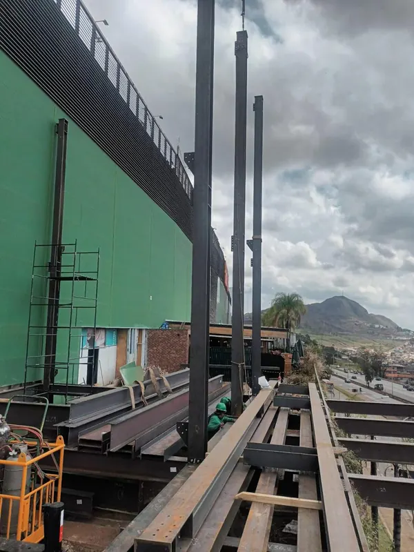 Pilares do elevador de carga erguidos junto à fachada, com a serra ao fundo