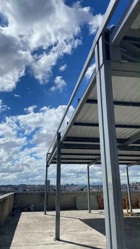 Pilar e vigas da cobertura contra o céu, com a cidade ao fundo