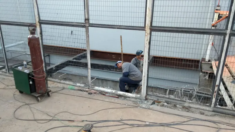 Soldador trabalhando na base da estrutura, junto à tela de proteção