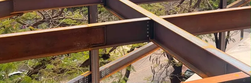 Vigas metálicas identificadas montadas na obra, entre as árvores