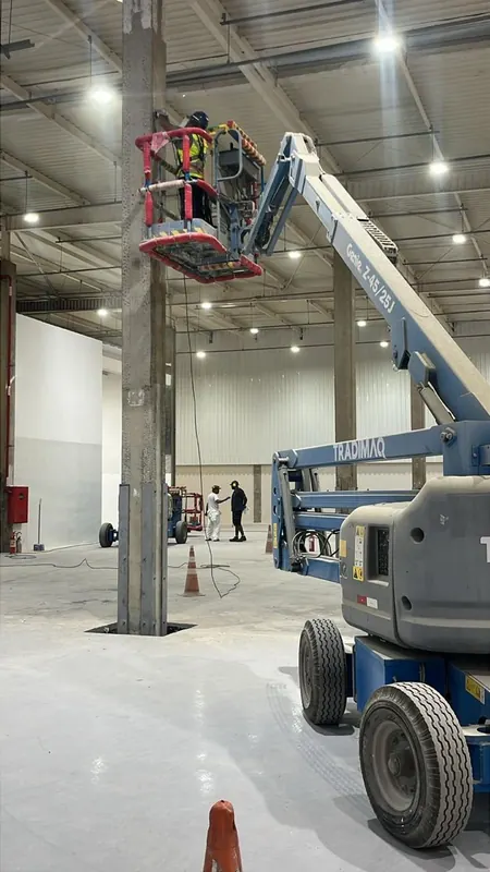 Montador em plataforma elevatória instalando o reforço na parte alta do pilar