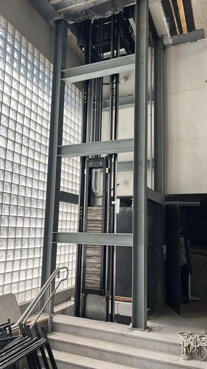 Torre metálica do elevador montada junto à parede de blocos de vidro, com as guias e a cabine instaladas