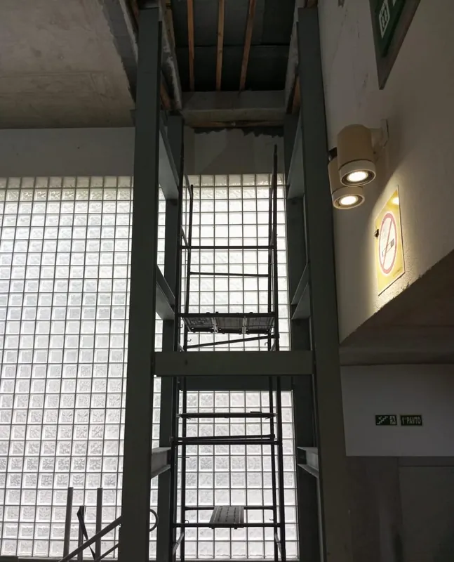 Torre metálica vista de frente, diante da parede de blocos de vidro