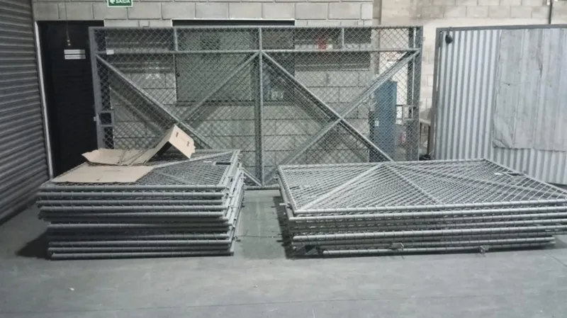 Portões tubulares pintados empilhados na fábrica, com um portão em pé ao fundo