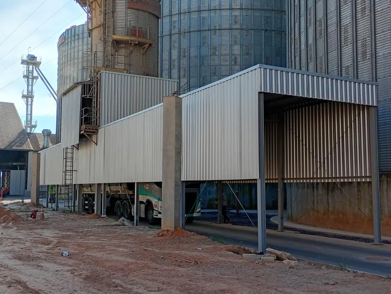 Cobertura e fechamento lateral concluídos junto aos silos, com caminhão na área de escoamento