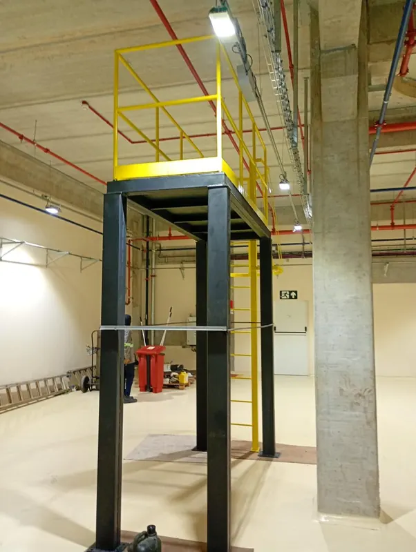 Plataforma metálica elevada com guarda-corpo amarelo ao lado de um pilar de concreto
